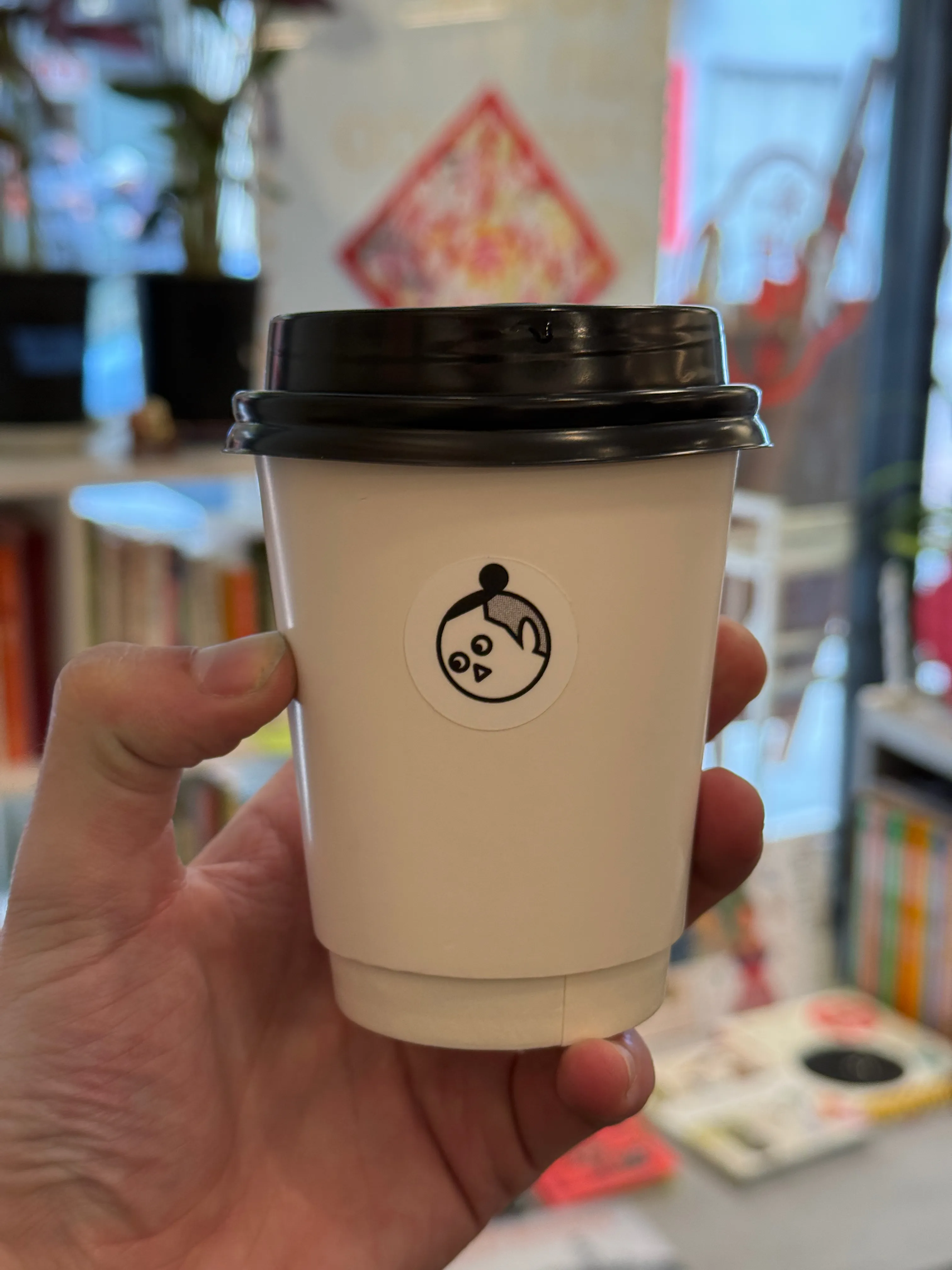 Front side of a coffee cup from Chen & Coffee, with a small cartoon face